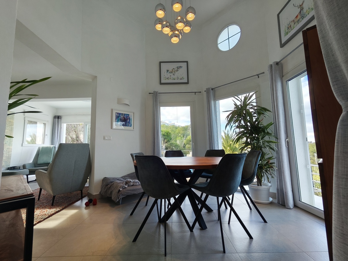 Modern dining area featuring a round wooden table, dark upholstered chairs, a chrome multi-light chandelier, and high ceilings with a circular accent window.