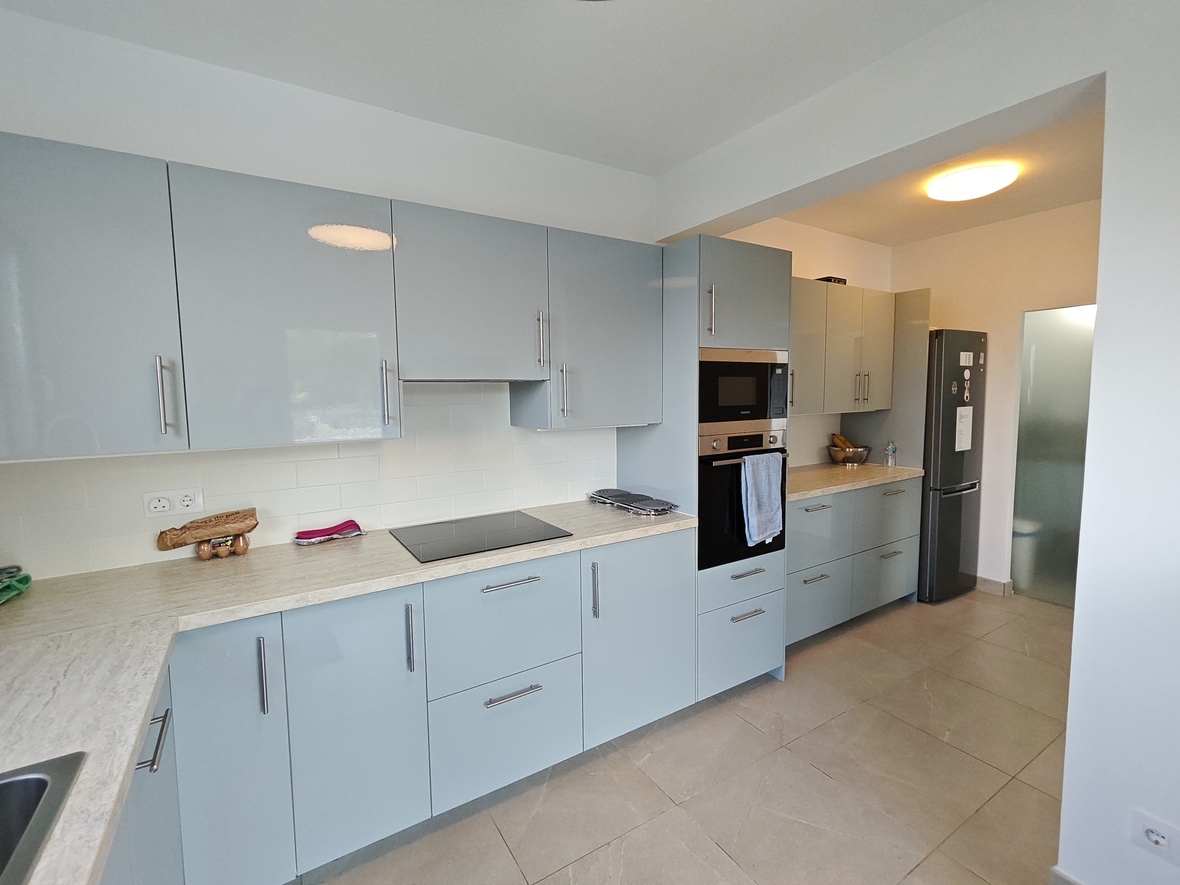 Modern kitchen featuring light blue high-gloss cabinetry, a stone-effect countertop, and integrated appliances with large-format beige floor tiles.