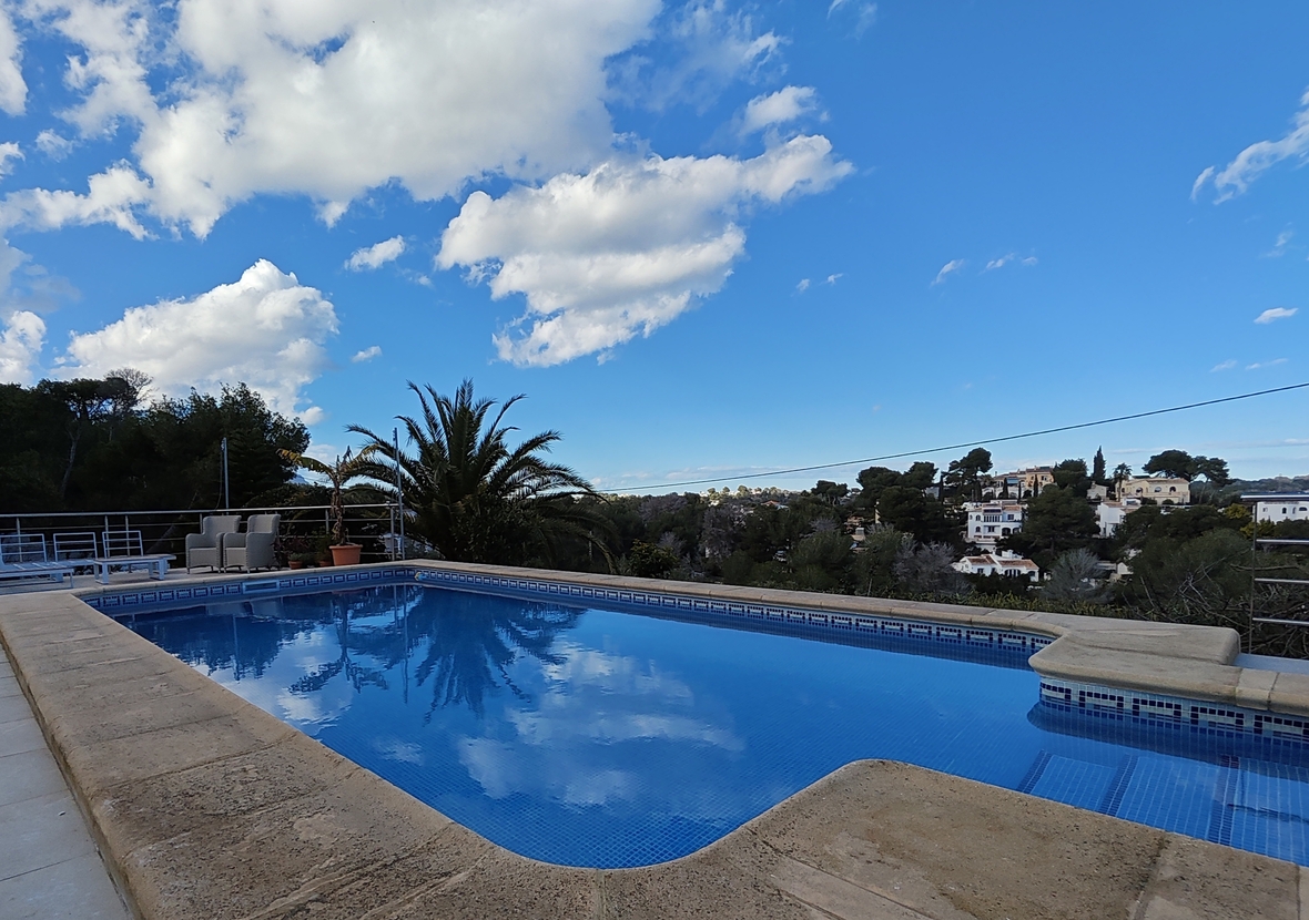 Outdoor swimming pool with blue mosaic tiles and stone coping, offering views of the surrounding Mediterranean landscape and residential area.