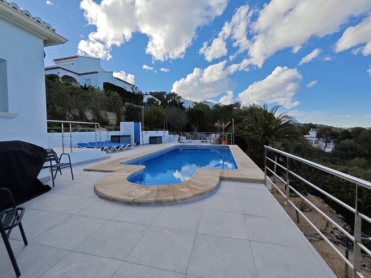 Outdoor swimming pool with stone coping, surrounded by a spacious tiled terrace and stainless steel railings overlooking a Mediterranean landscape.