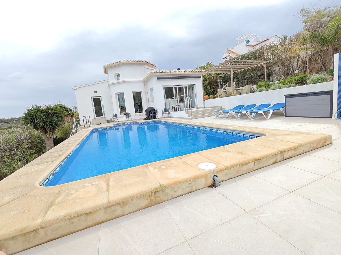 Private rectangular pool with blue tiling and stone coping, surrounded by a light-tiled terrace with sun loungers and a white Mediterranean villa.