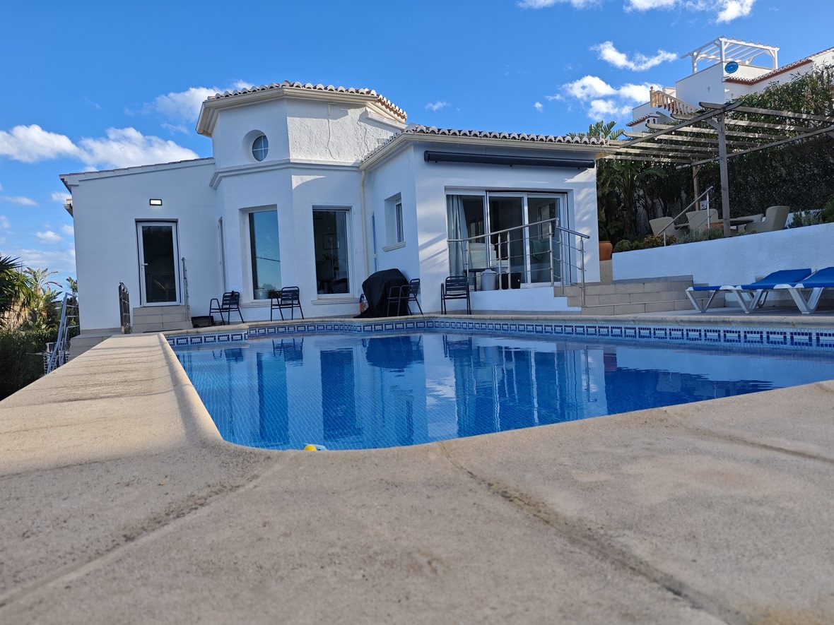Private swimming pool with blue mosaic tiling and stone surround, set against a white Mediterranean villa featuring an octagonal turret and sliding glass doors.