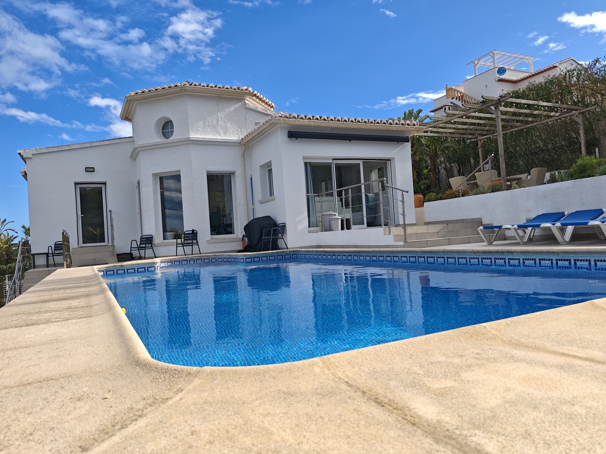 Private swimming pool with blue mosaic tiling, surrounded by a stone terrace and a white-washed villa featuring a distinctive circular tower element.