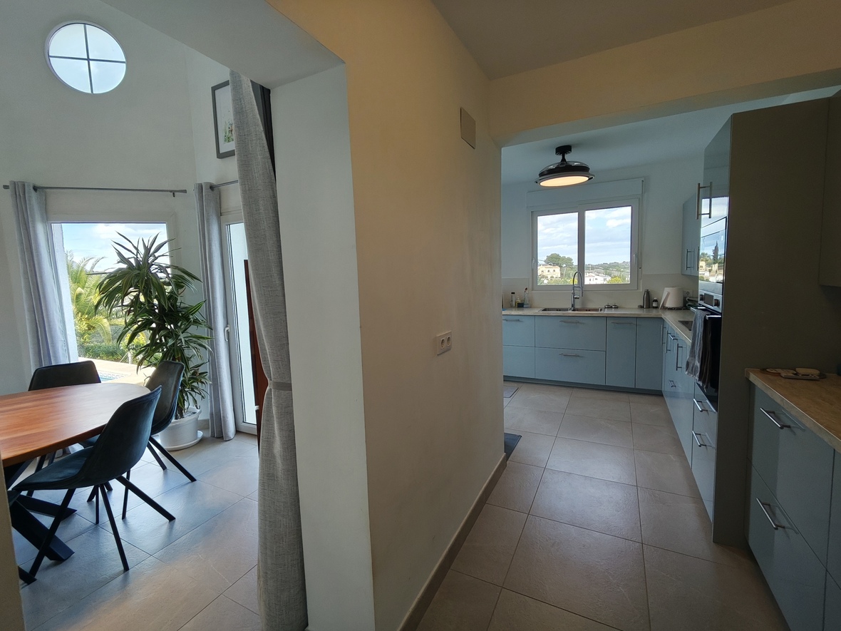 Transition between a bright dining area with wooden furniture and a modern kitchen featuring light blue cabinetry and integrated appliances.