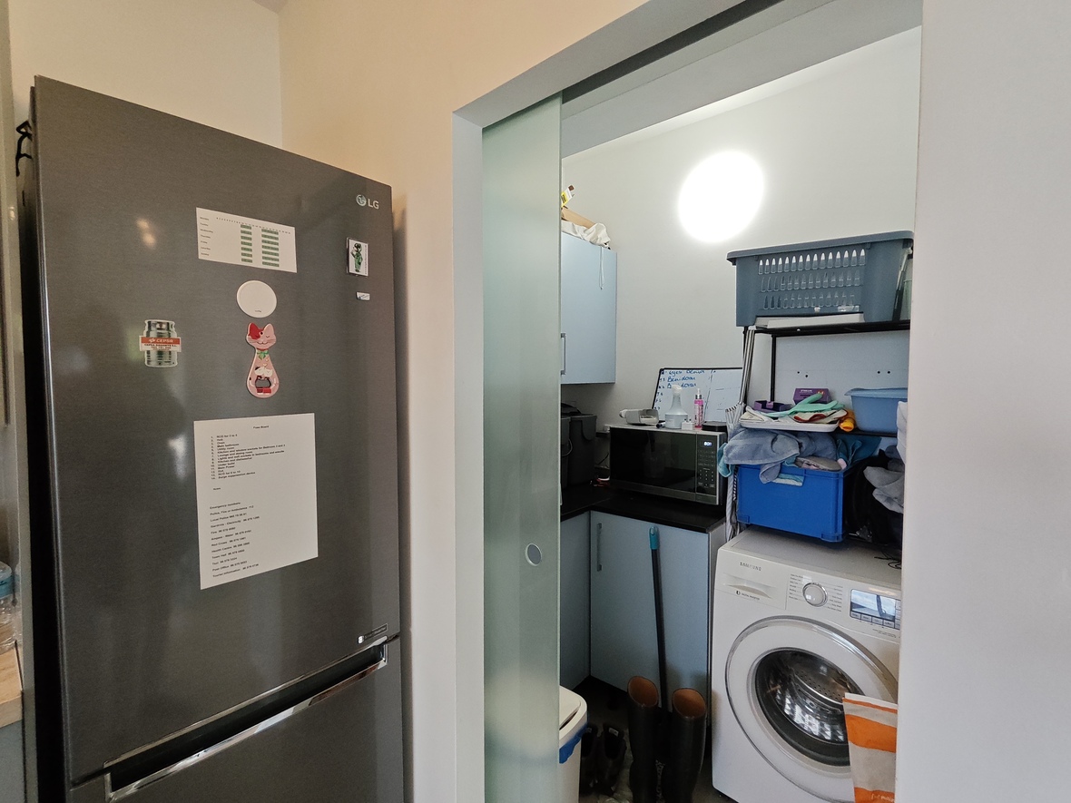 Utility room featuring a frosted glass sliding door, equipped with a Samsung washing machine, microwave, and light blue cabinetry next to an LG refrigerator.