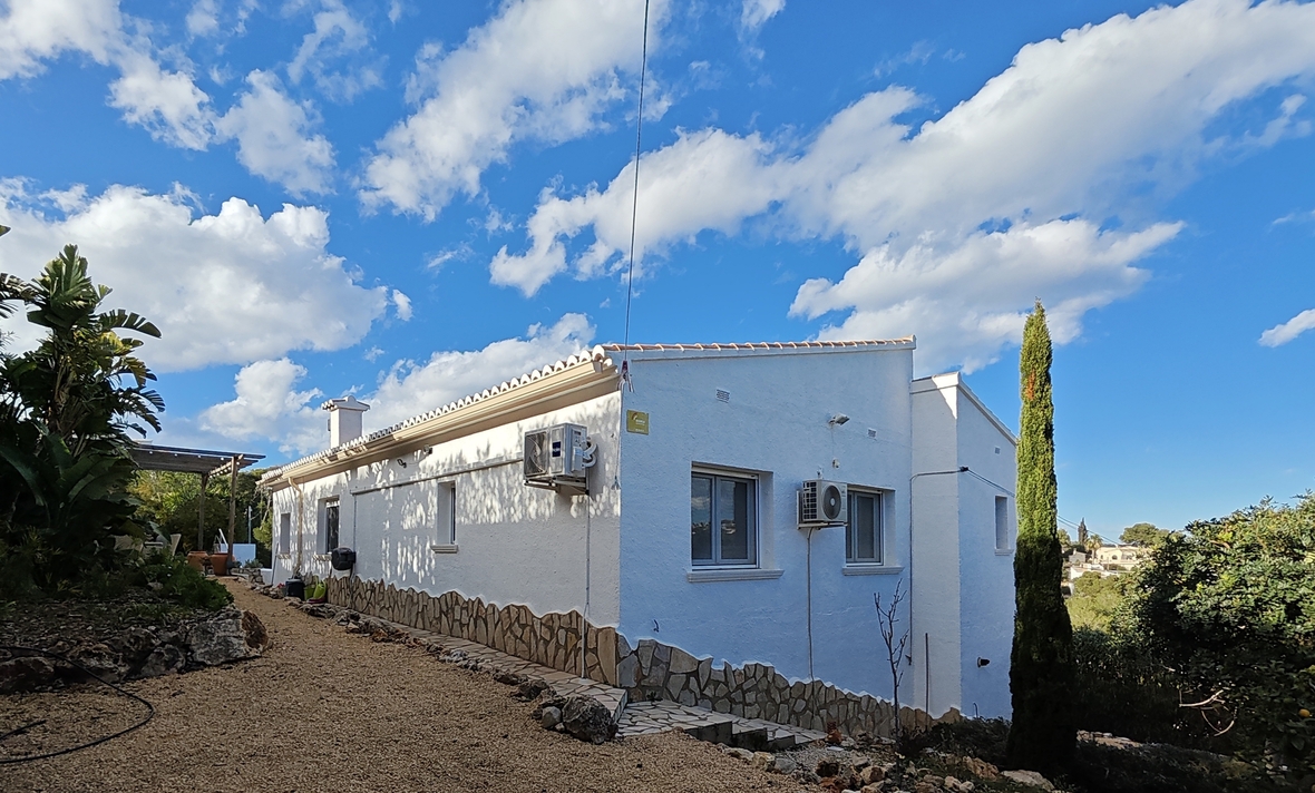 White villa exterior featuring natural stone cladding, gravel pathway, and Mediterranean landscaping under a bright blue sky.