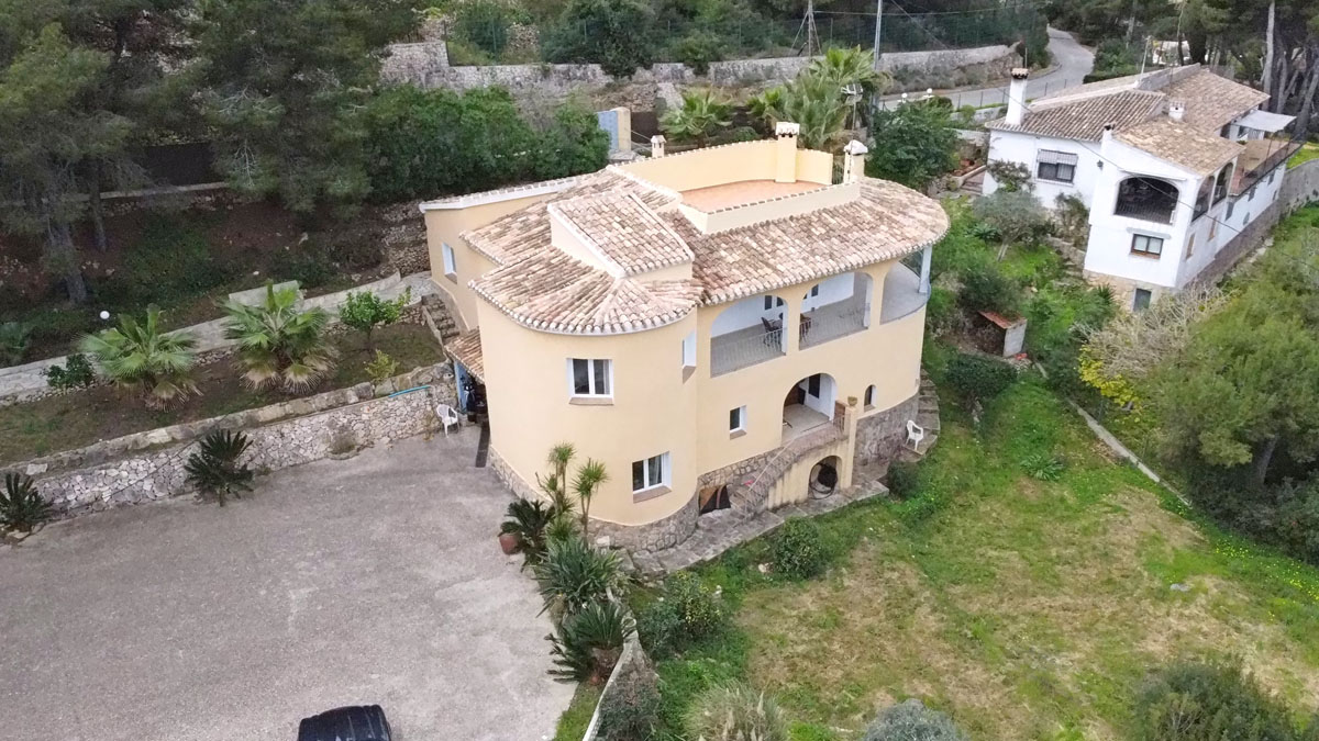 Aerial view of the Mediterranean villa featuring a curved facade, terracotta tile roofing, and a spacious paved driveway set within a landscaped plot.