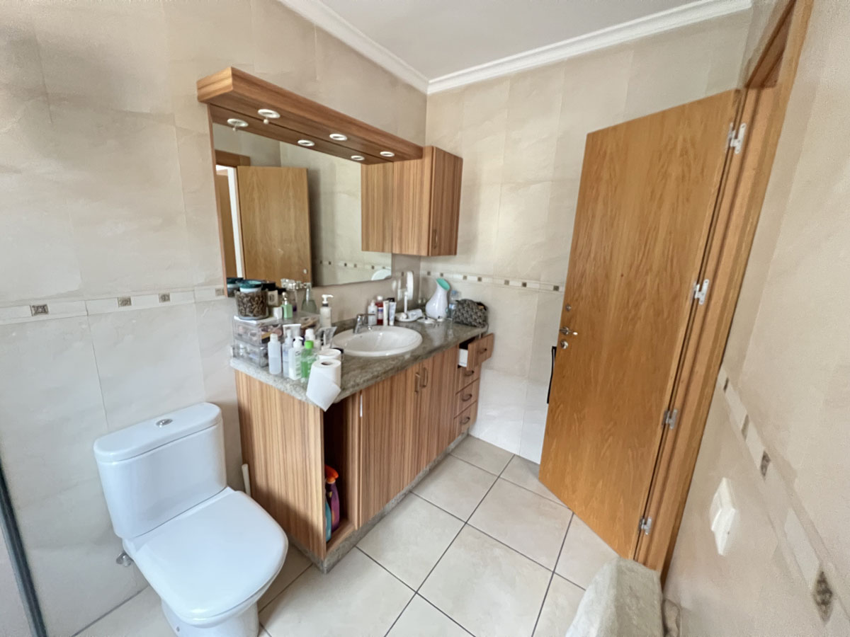 Bathroom featuring a wooden vanity with a stone countertop and integrated sink. The space includes cream-toned wall tiles and a mirror with overhead lighting.