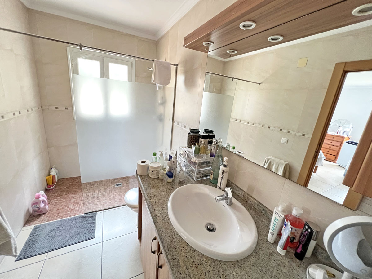 Bathroom with a granite countertop, oval sink, and wooden vanity. Features a walk-in shower with a frosted glass partition and reddish mosaic tile flooring.