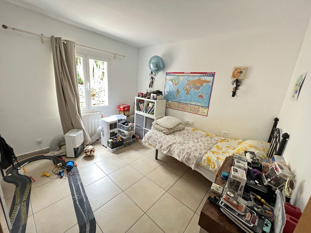 Bedroom featuring ceramic tile flooring, a radiator, and a window for natural light. The room offers a functional layout with neutral white walls.