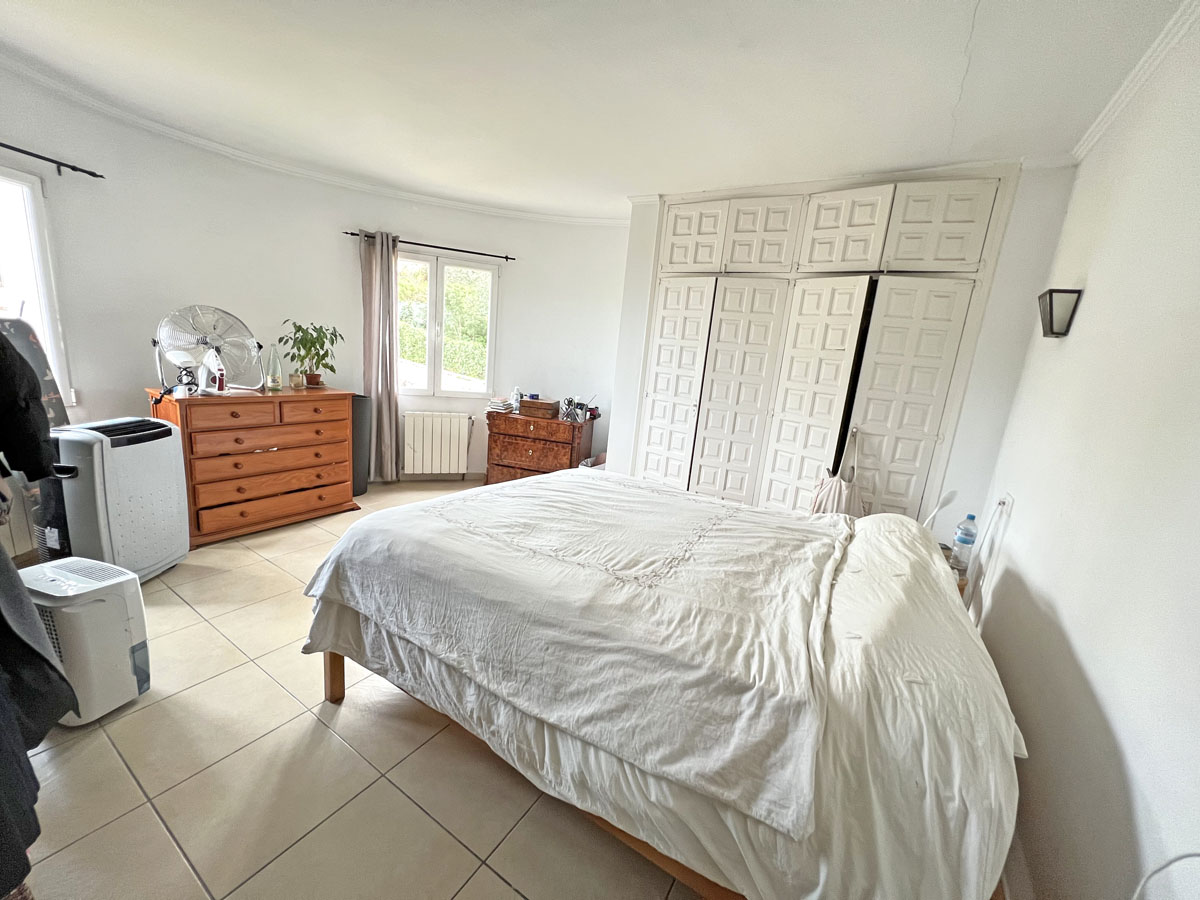 Bedroom featuring extensive floor-to-ceiling built-in wardrobes with decorative panels, tiled flooring, and natural light from a side window.