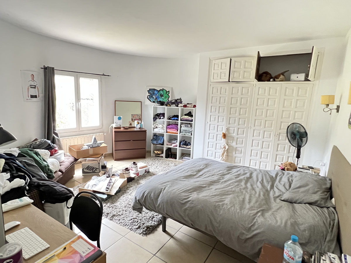 Bedroom featuring large white paneled built-in wardrobes, tiled flooring, and a window providing natural light and ventilation.