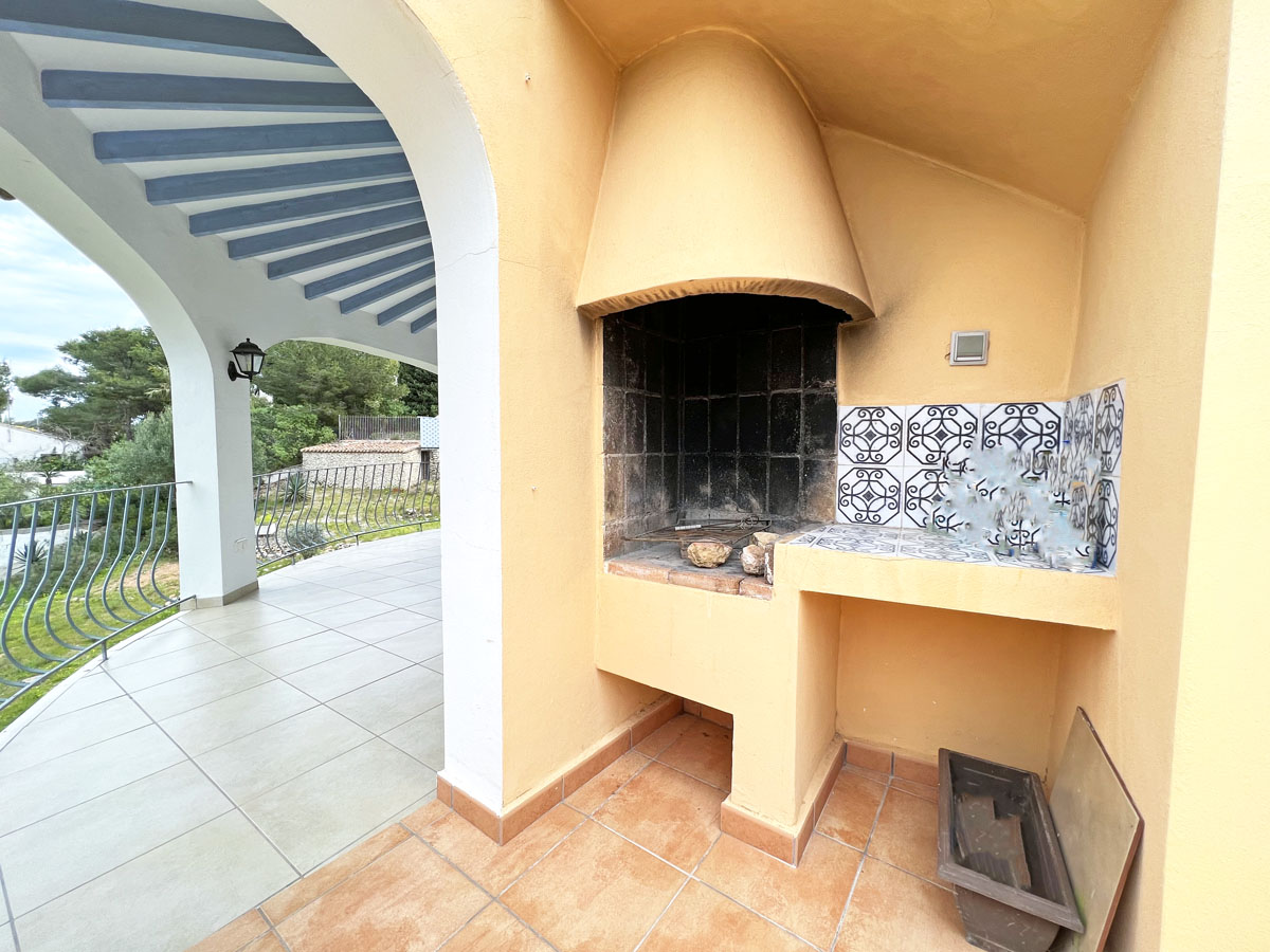 Built-in masonry barbecue featuring a conical hood and decorative tiled counter, located on a covered terrace with white arches and blue ceiling beams.