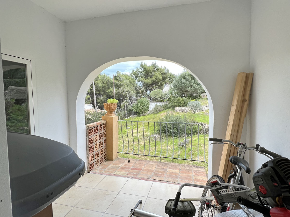 Covered porch featuring a traditional Mediterranean archway with views of the garden. Functional space with ceramic tiling and a metal safety railing.