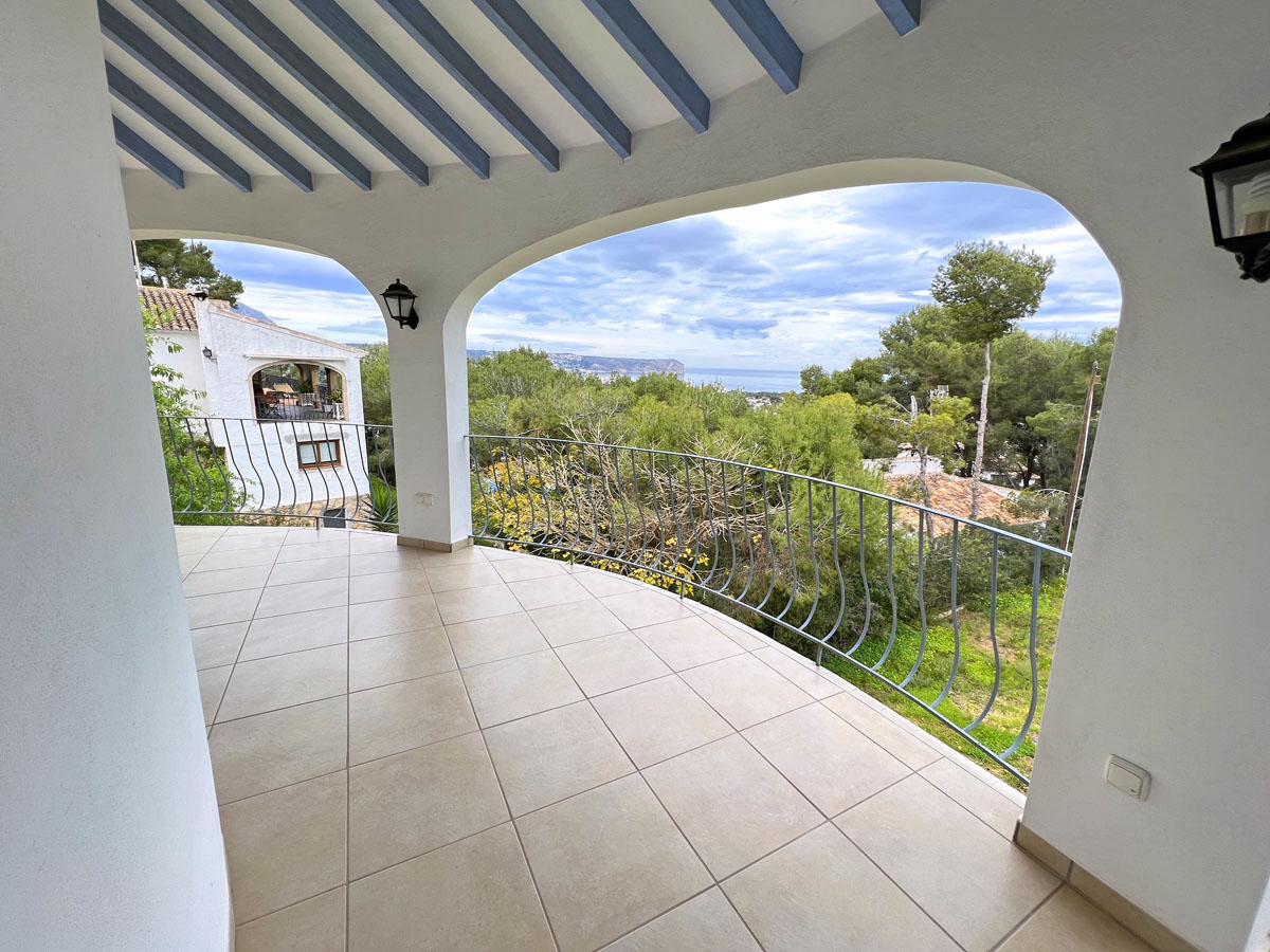 Covered terrace featuring blue wooden ceiling beams, tiled flooring, and curved iron railings with panoramic views of the sea and Cabo San Antonio.
