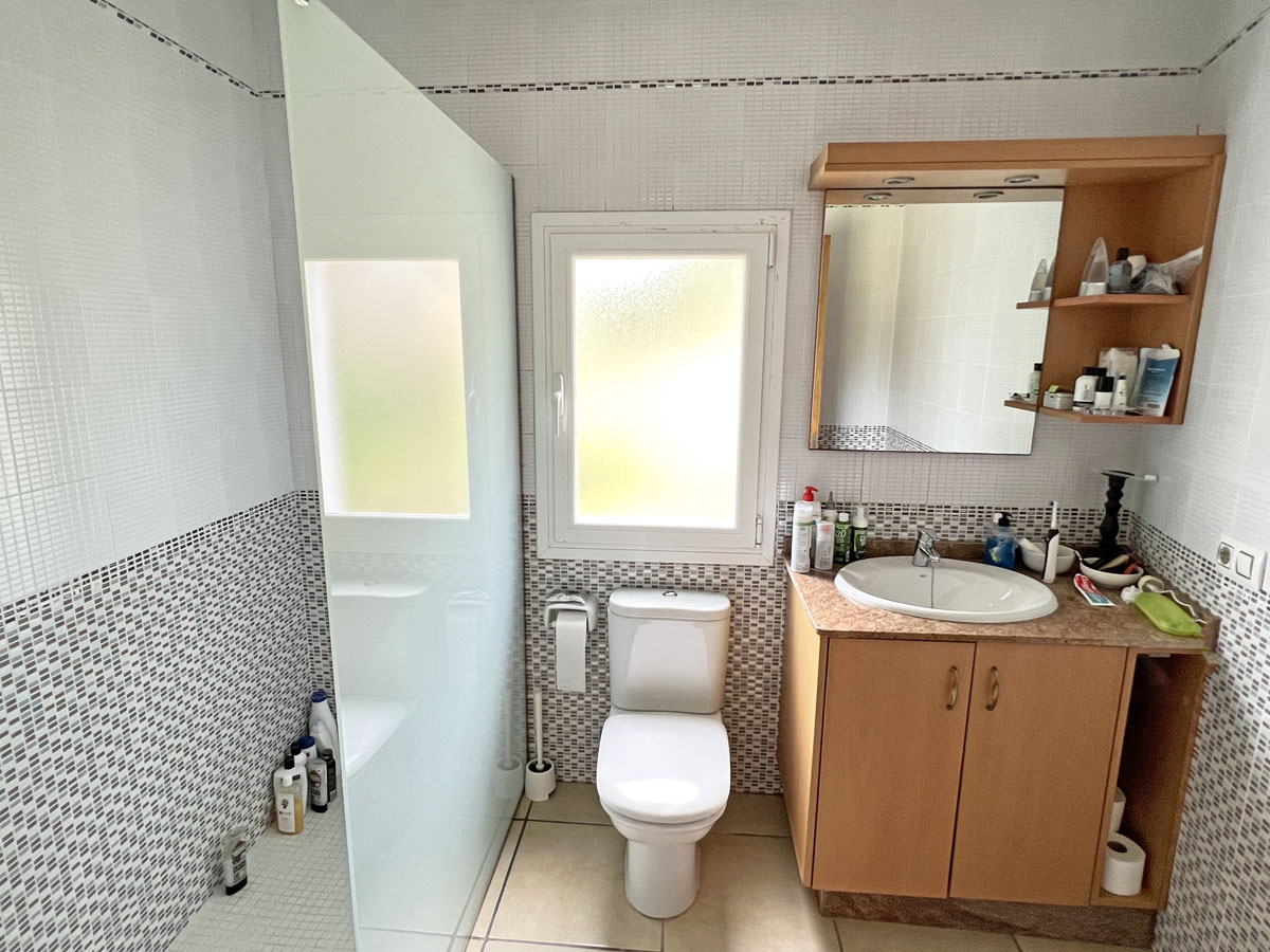 Functional bathroom featuring a walk-in shower with frosted glass, a wooden vanity with marble-effect countertop, and decorative mosaic wall tiling.