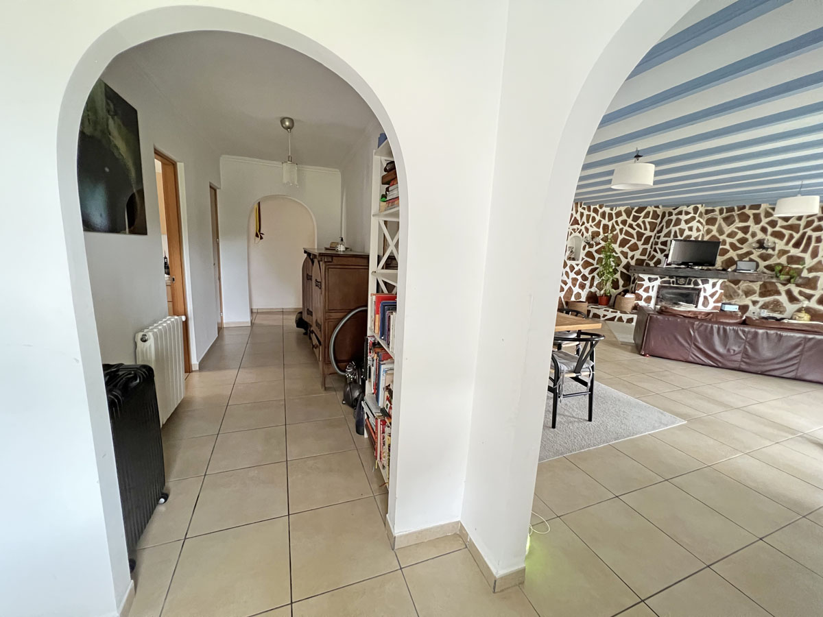 Hallway featuring traditional arches leading to a living area with a blue-striped ceiling and a characteristic natural stone wall with a fireplace.