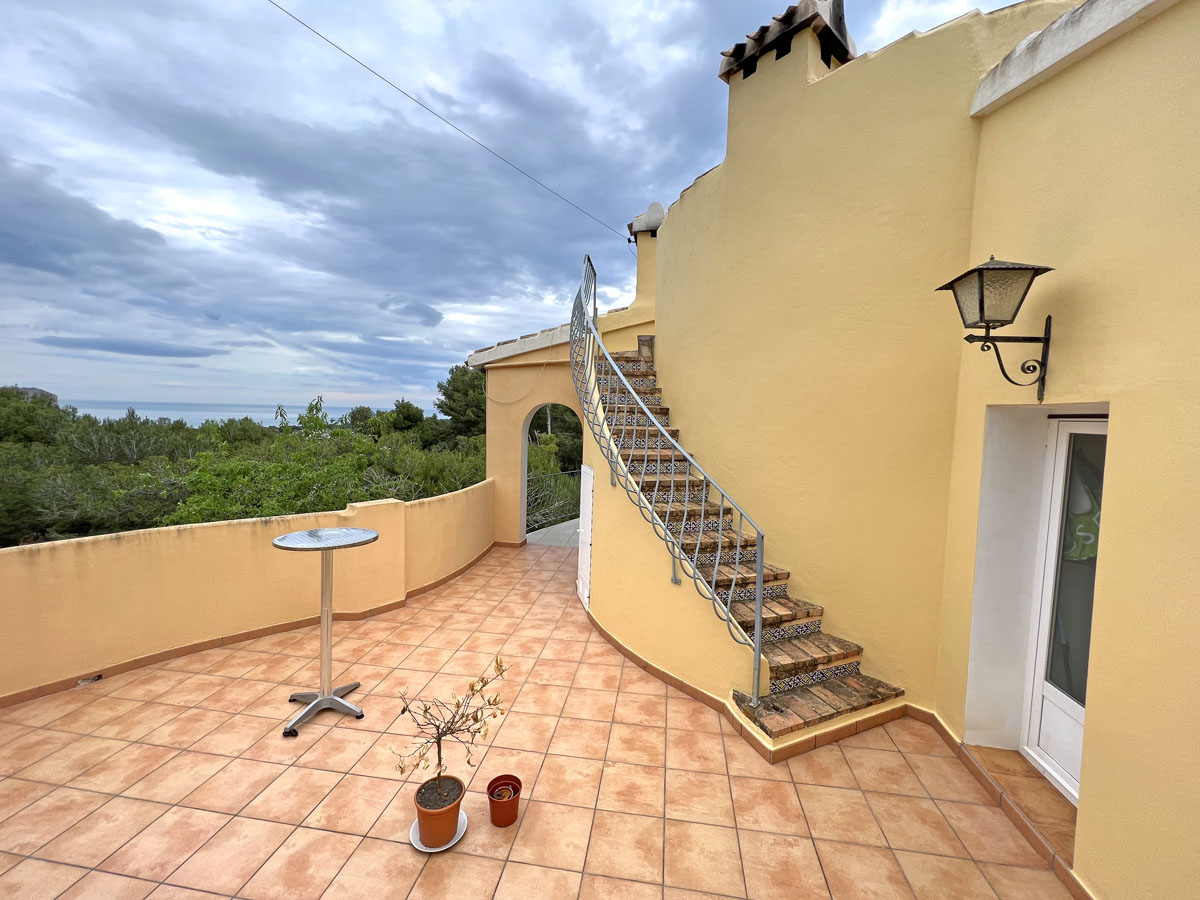 Outdoor terrace featuring terracotta tiling and a curved staircase with decorative tile risers. The space offers elevated views of the Mediterranean Sea and pine forests.