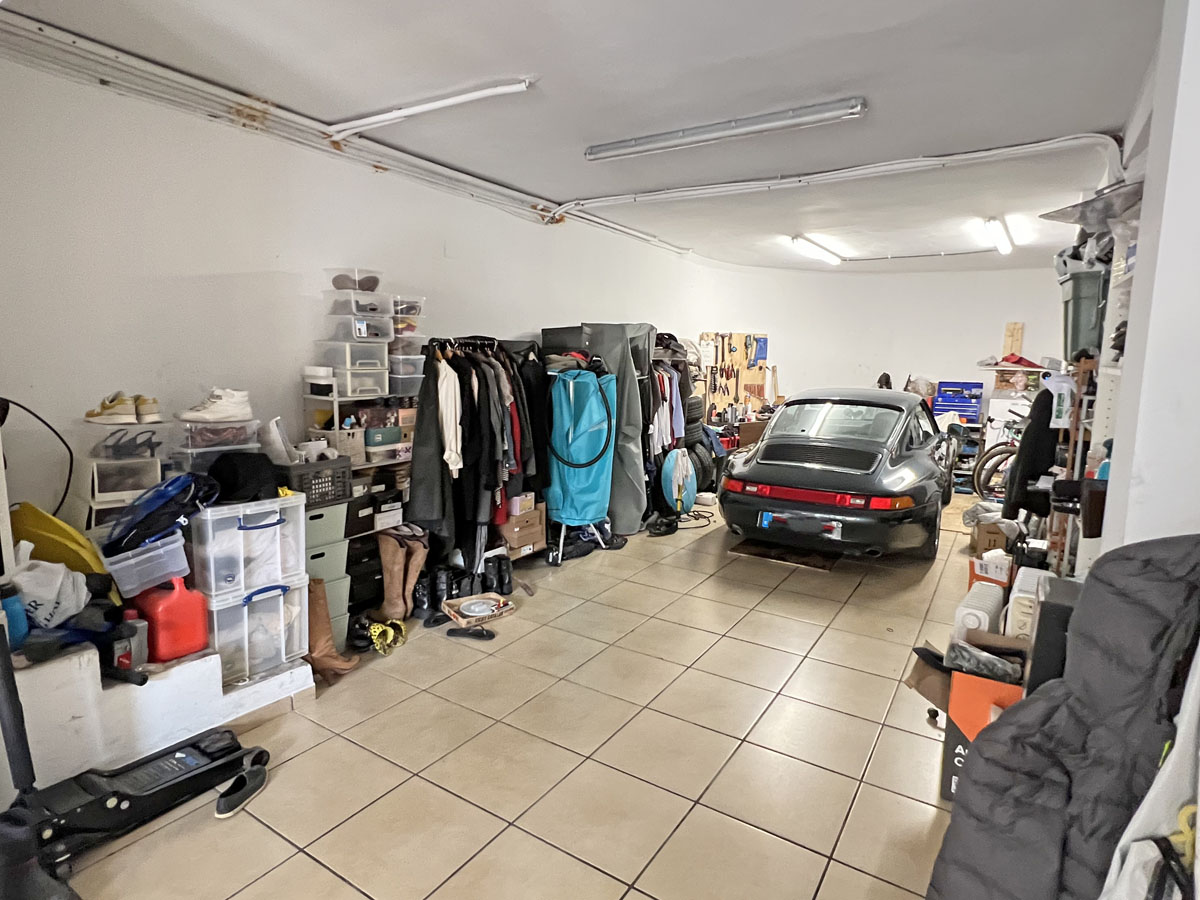 Spacious garage with ceramic tile flooring, fluorescent tube lighting, and multiple shelving units and racks for organized storage.