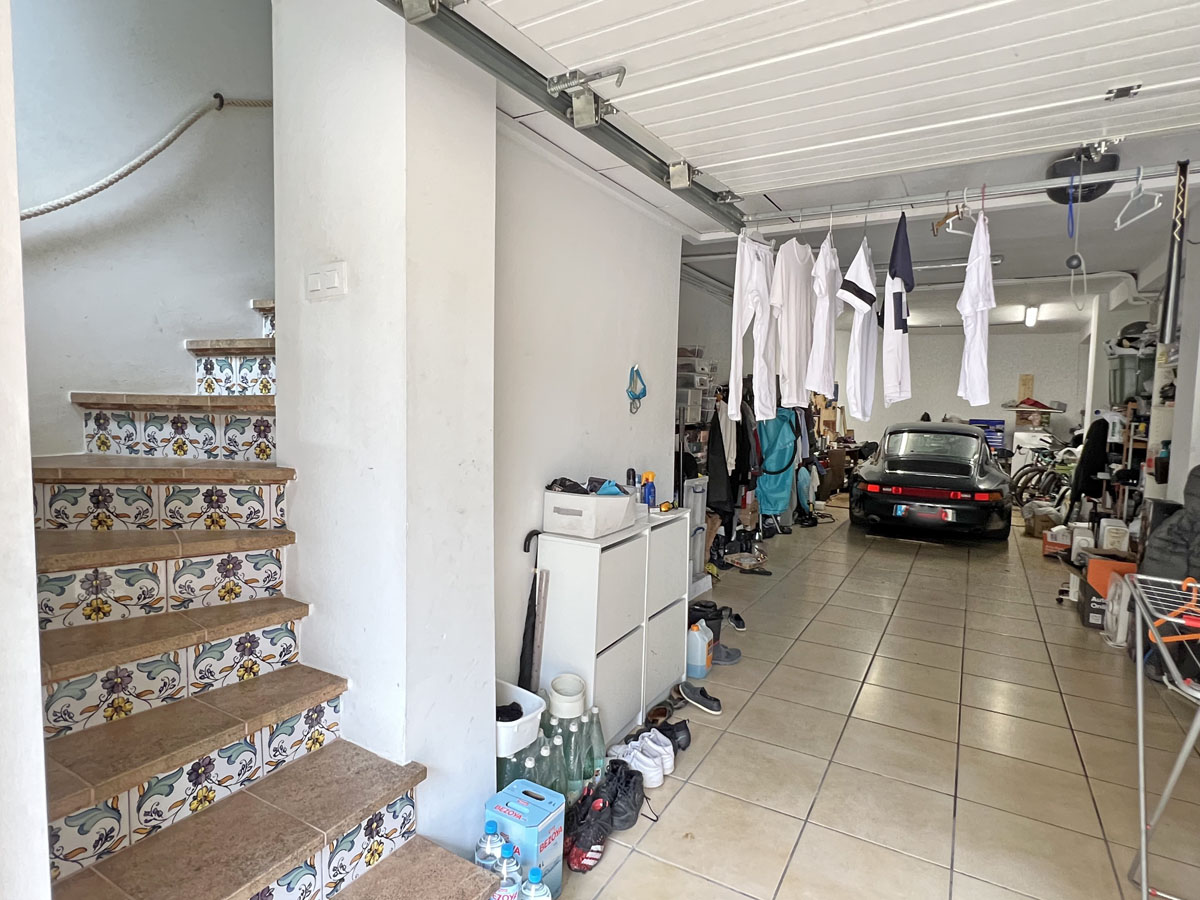 Spacious garage with tiled flooring and storage area, featuring an internal staircase with traditional Mediterranean tilework leading to the main house.