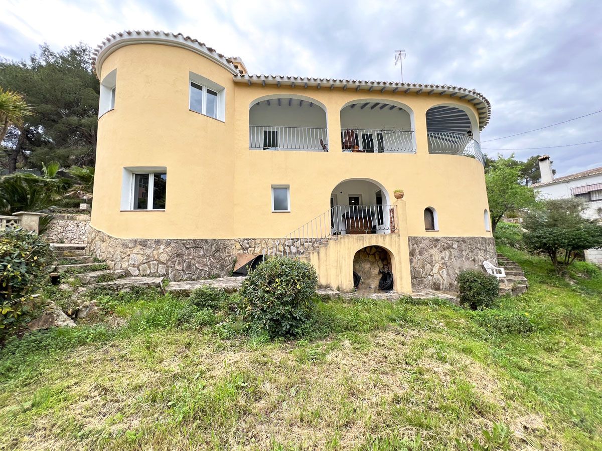 Two-story Mediterranean villa featuring a yellow facade, natural stone base, circular architectural elements, and arched terraces with metal railings.