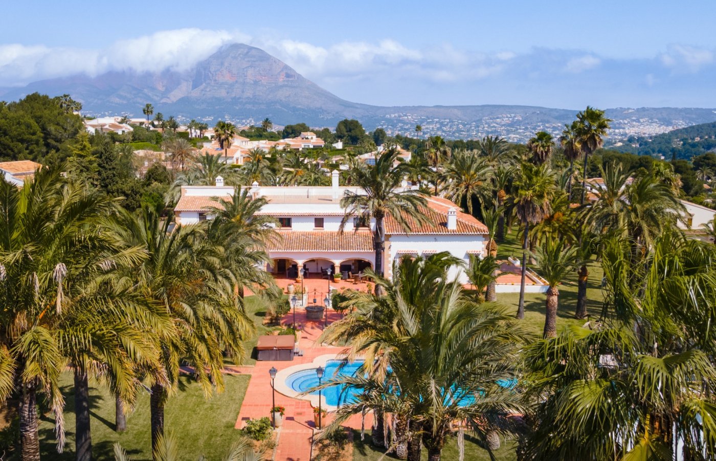 Aerial view of the Mediterranean villa featuring a large swimming pool, extensive palm gardens, and panoramic views of the Montgó mountain.