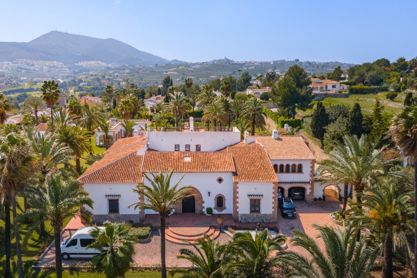 Aerial view of the Mediterranean villa featuring terracotta tiled roofs, Tosca stone arches, and an expansive plot with palm trees and panoramic valley views.
