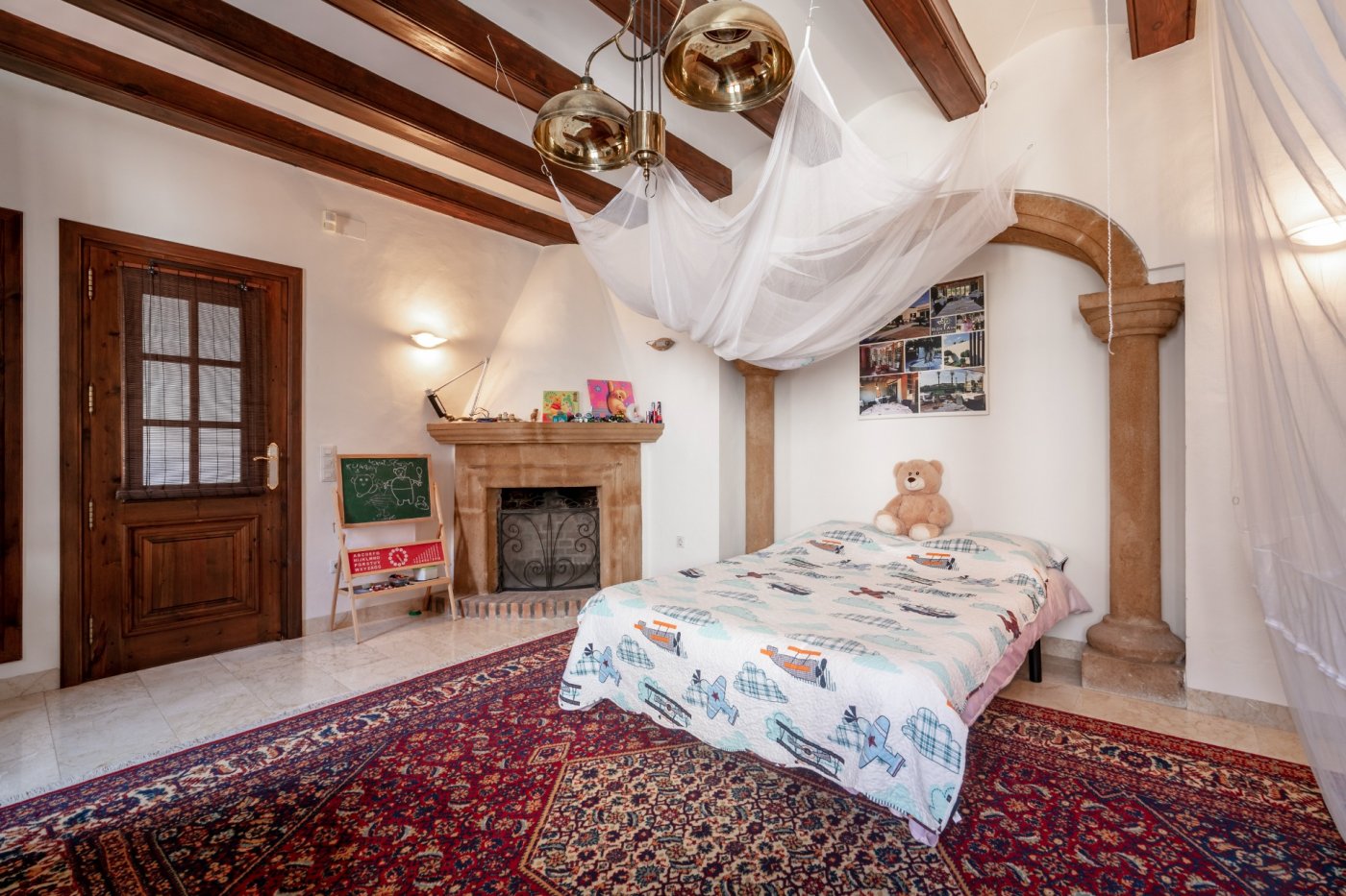 Bedroom featuring exposed wooden beams, a Tosca stone fireplace, and an architectural arch, finished with marble floors and a classic patterned rug.