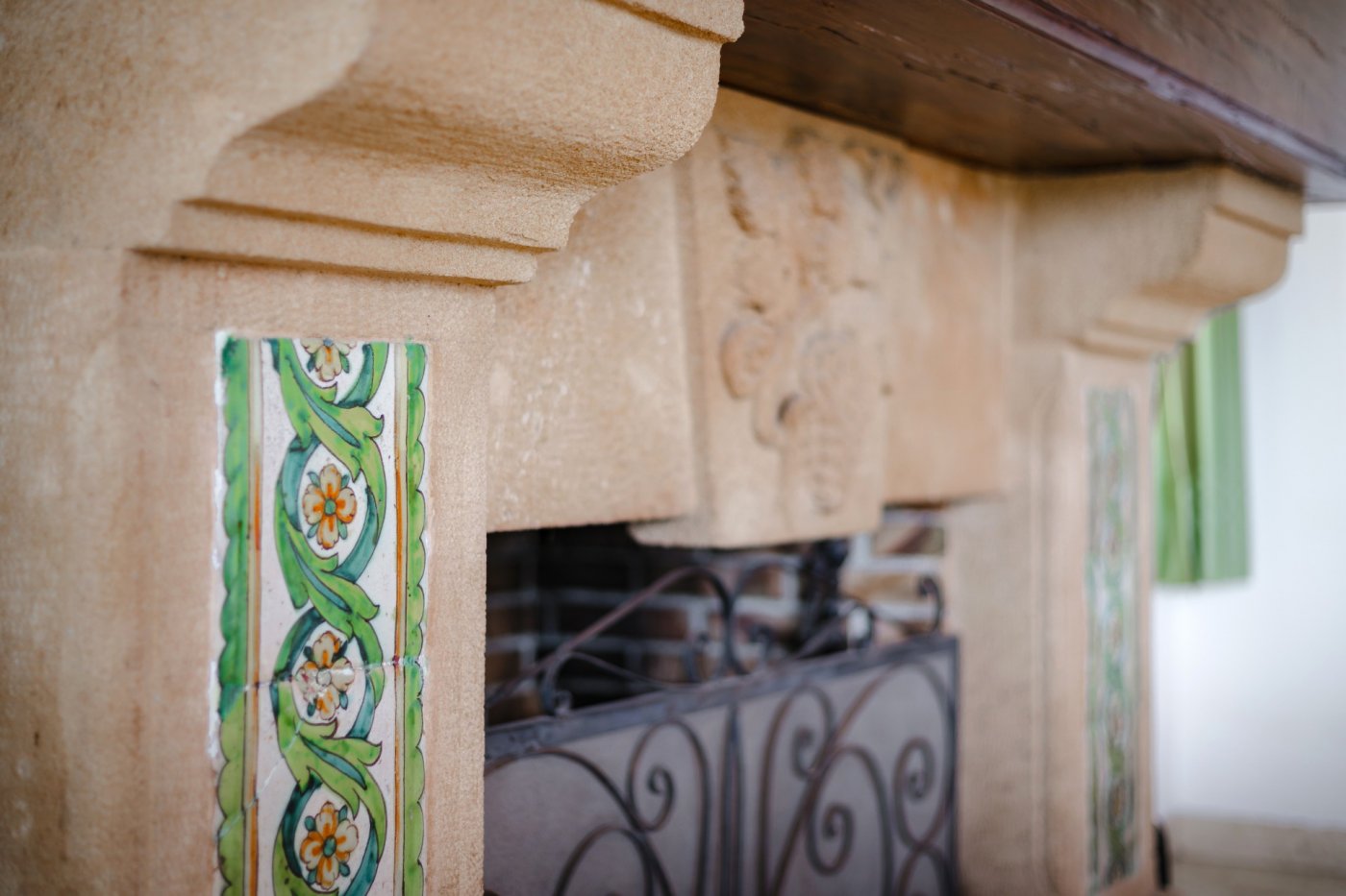 Close-up of a traditional Tosca stone fireplace featuring hand-painted ceramic tiles and a dark solid wood mantelpiece.