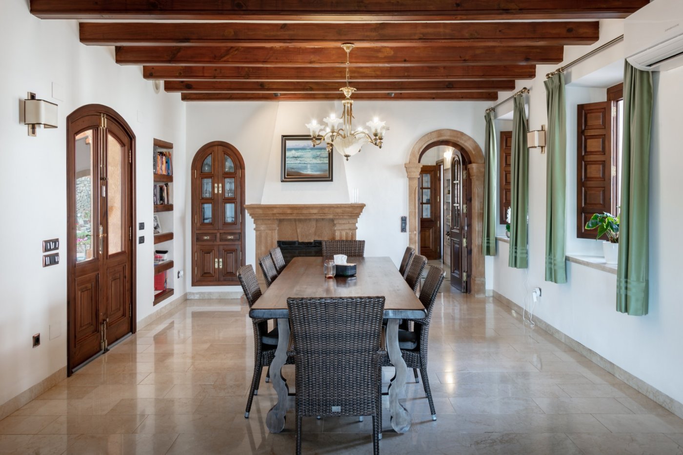 Dining area featuring exposed wooden beams, a Tosca stone fireplace, and marble floors. The space is defined by natural stone arches and a large wooden table.