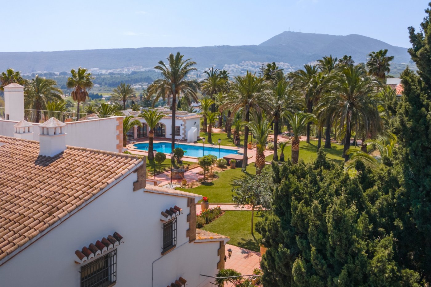 Elevated perspective of the Mediterranean grounds, highlighting the 16x7m pool, guest house, and lush palm garden with panoramic valley and mountain views.