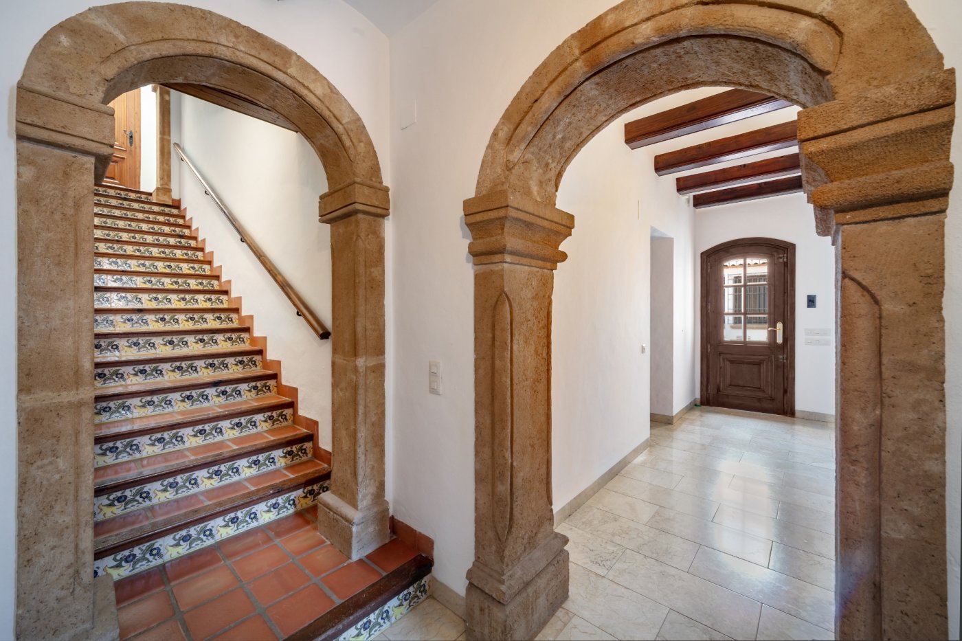 Entrance hall featuring hand-carved stone arches, a staircase with traditional tiled risers, and exposed wooden ceiling beams.