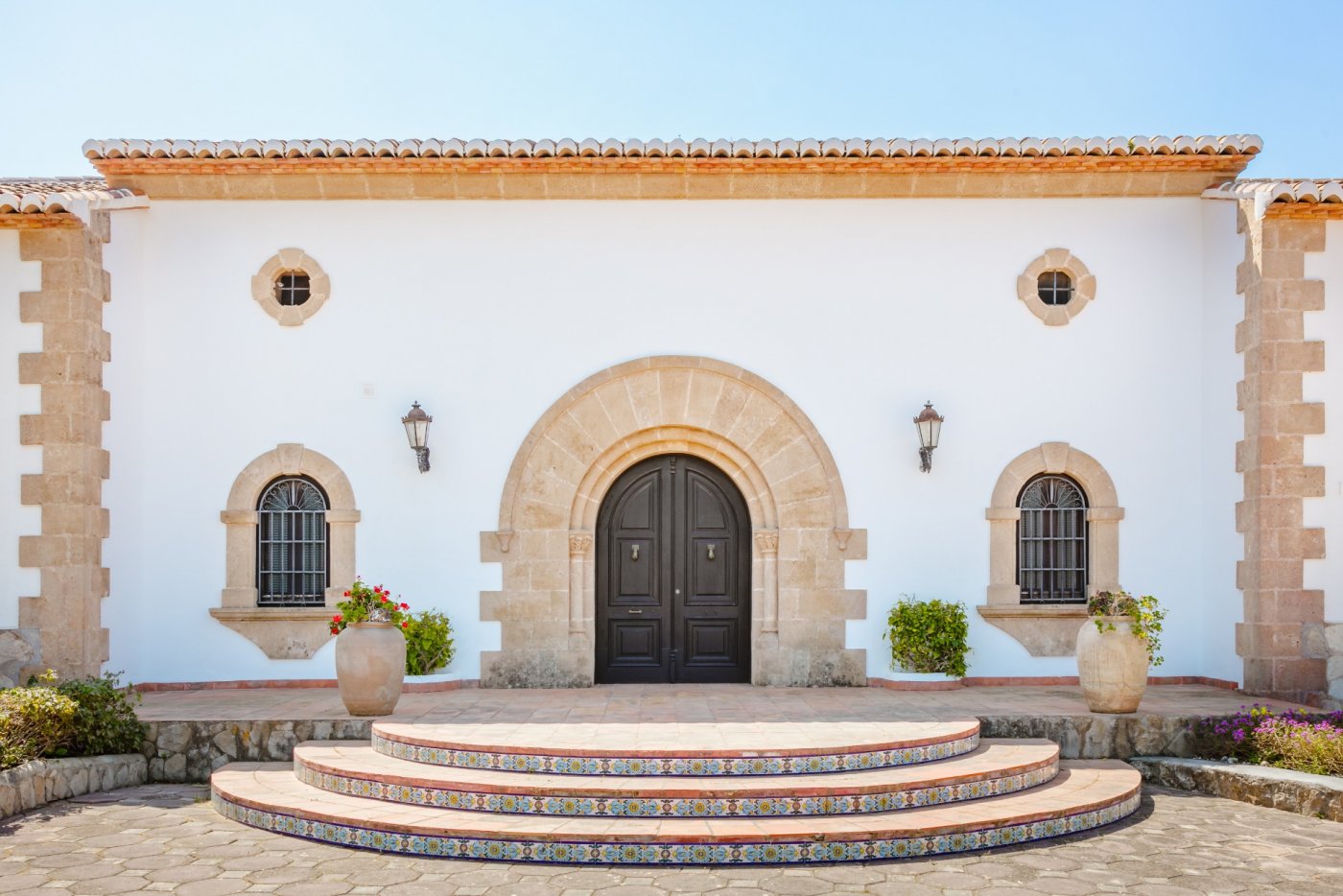 Main entrance featuring a Tosca stone arch, dark wood double doors, and semicircular terracotta steps with traditional decorative tile risers.