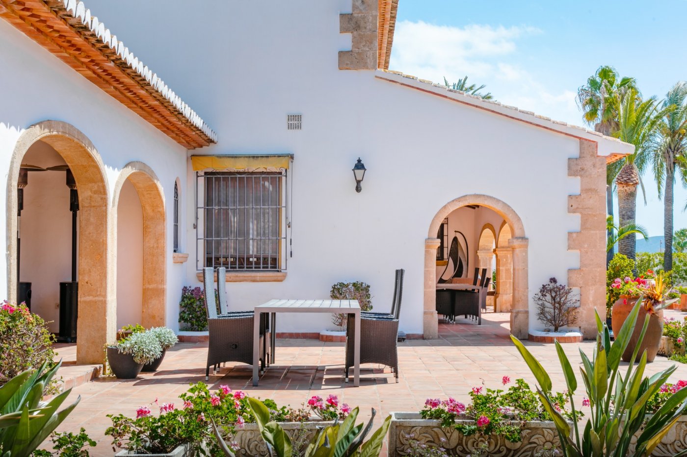 Outdoor terrace featuring traditional Tosca stone arches, terracotta tiling, and an al fresco dining area set against a white Mediterranean facade.