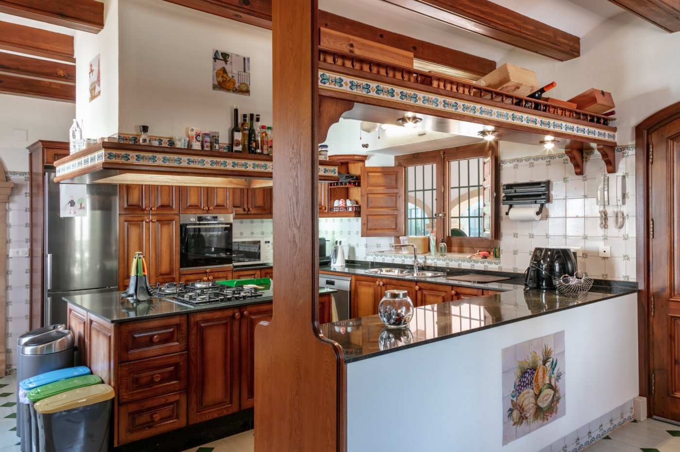 Rustic kitchen featuring exposed wooden beams, dark granite countertops, and traditional patterned tiles. It includes a central island with a gas hob.