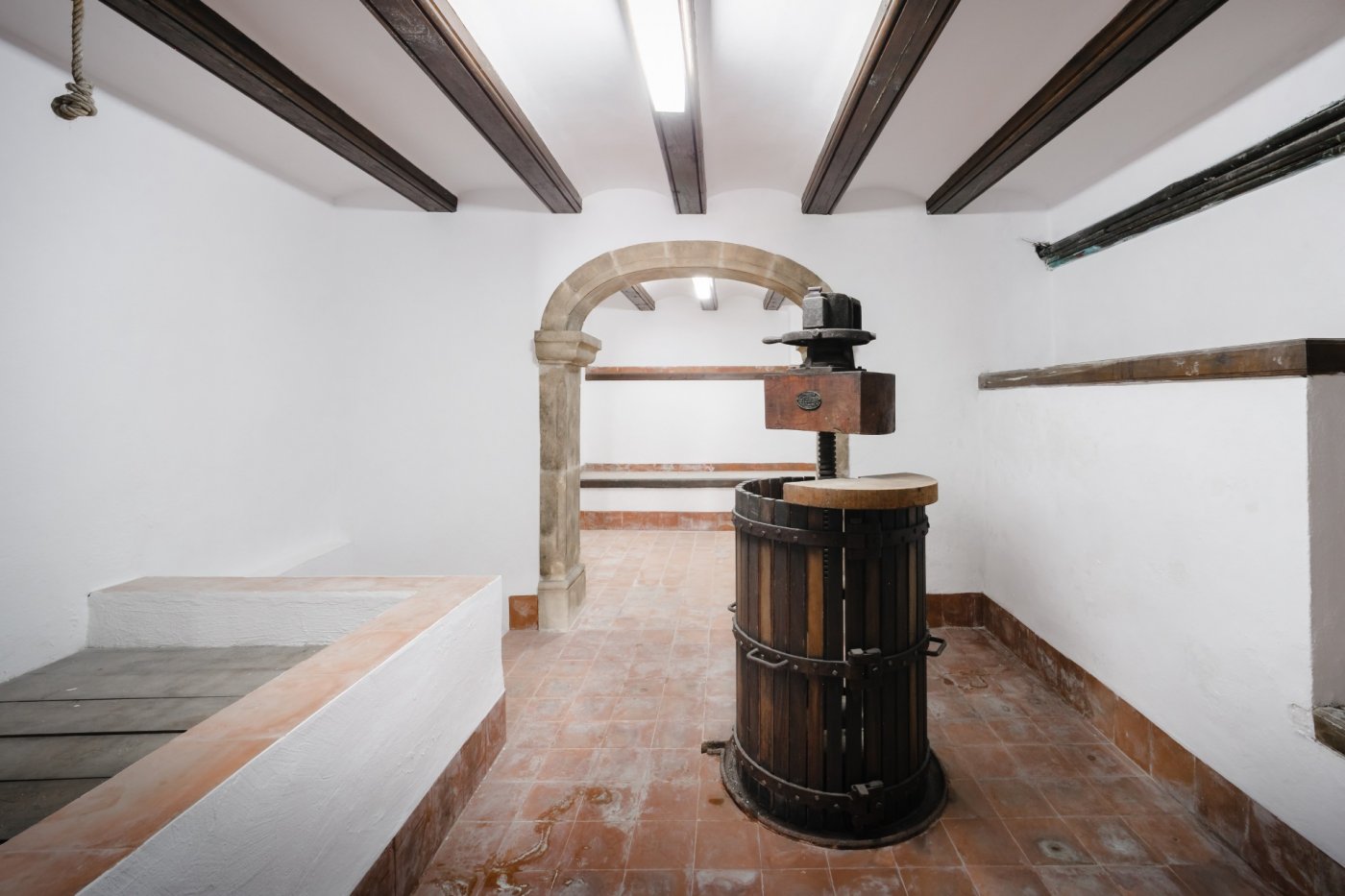 Traditional wine cellar featuring a vintage wooden wine press, terracotta tile flooring, dark ceiling beams, and an authentic Tosca stone archway.