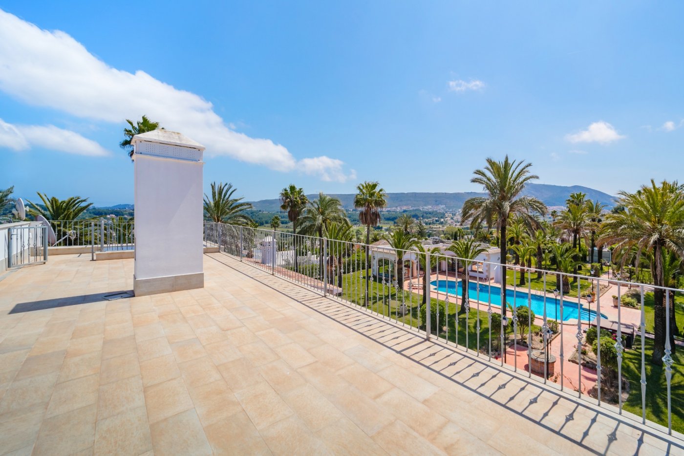 Upper terrace featuring tiled flooring and metal railings, overlooking the expansive palm garden, large swimming pool, and scenic valley views.