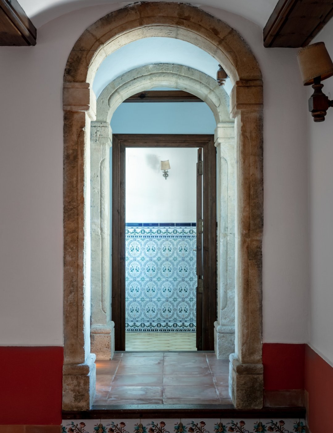 View through natural Tosca stone arches leading to a room with traditional decorative wall tiles and terracotta flooring.