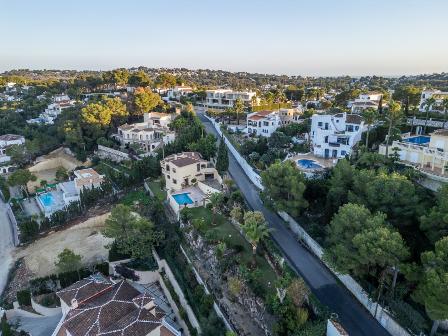 Aerial view of the Costa Nova Panorama neighborhood, featuring Mediterranean villas with private pools, terracotta roofs, and lush pine-covered hillsides.
