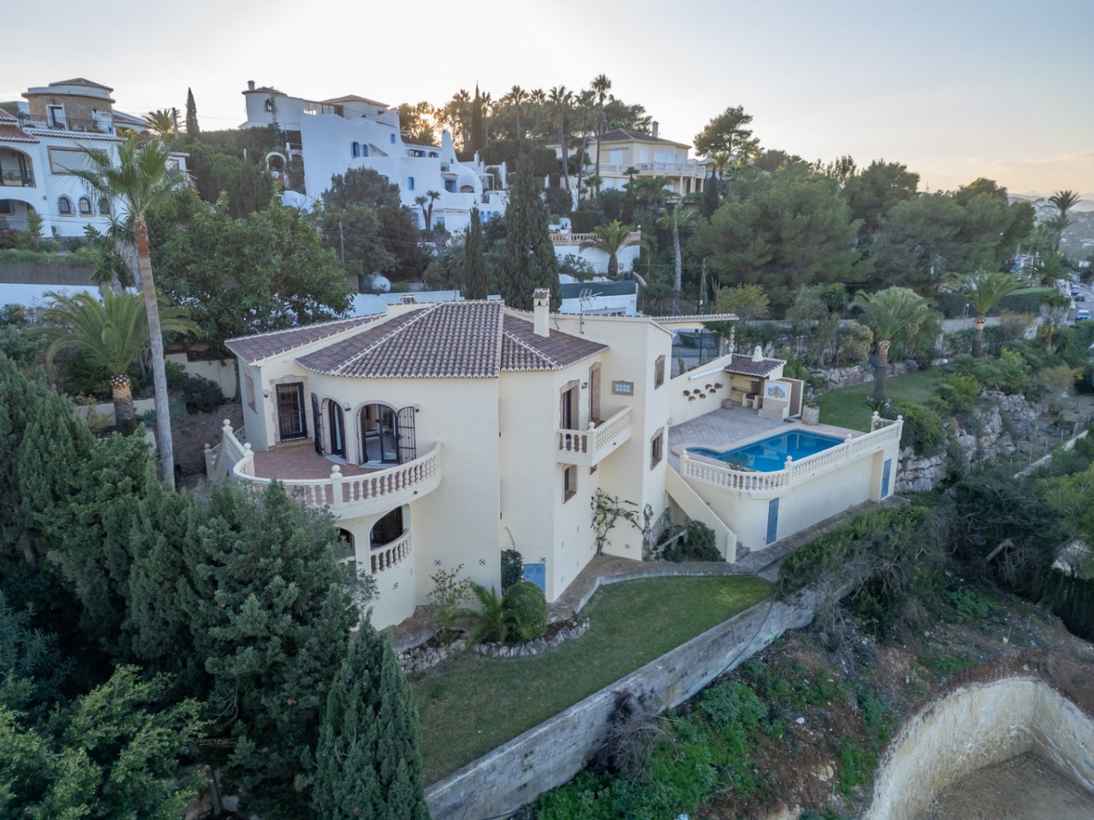 Aerial view of the Mediterranean villa featuring balustraded terraces, a rectangular swimming pool, and an outdoor BBQ area set within landscaped gardens.