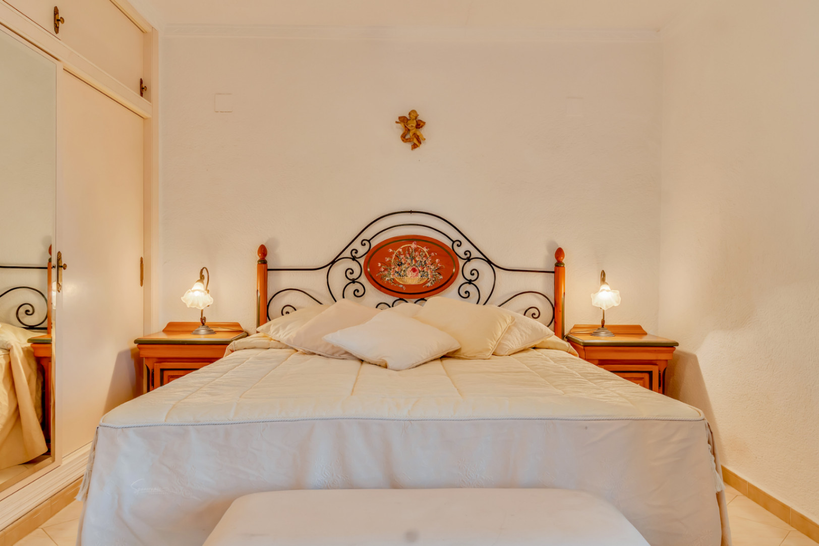 Bedroom featuring a double bed with a decorative wrought iron headboard and wooden nightstands. A built-in wardrobe with a mirrored door is visible.