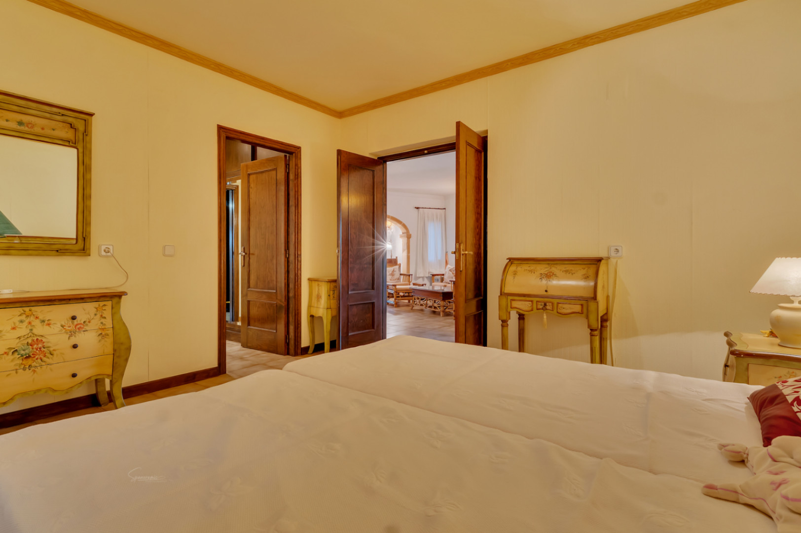 Bedroom featuring hand-painted vintage furniture, solid wood doors, and a view through to the living area with traditional stone archways.