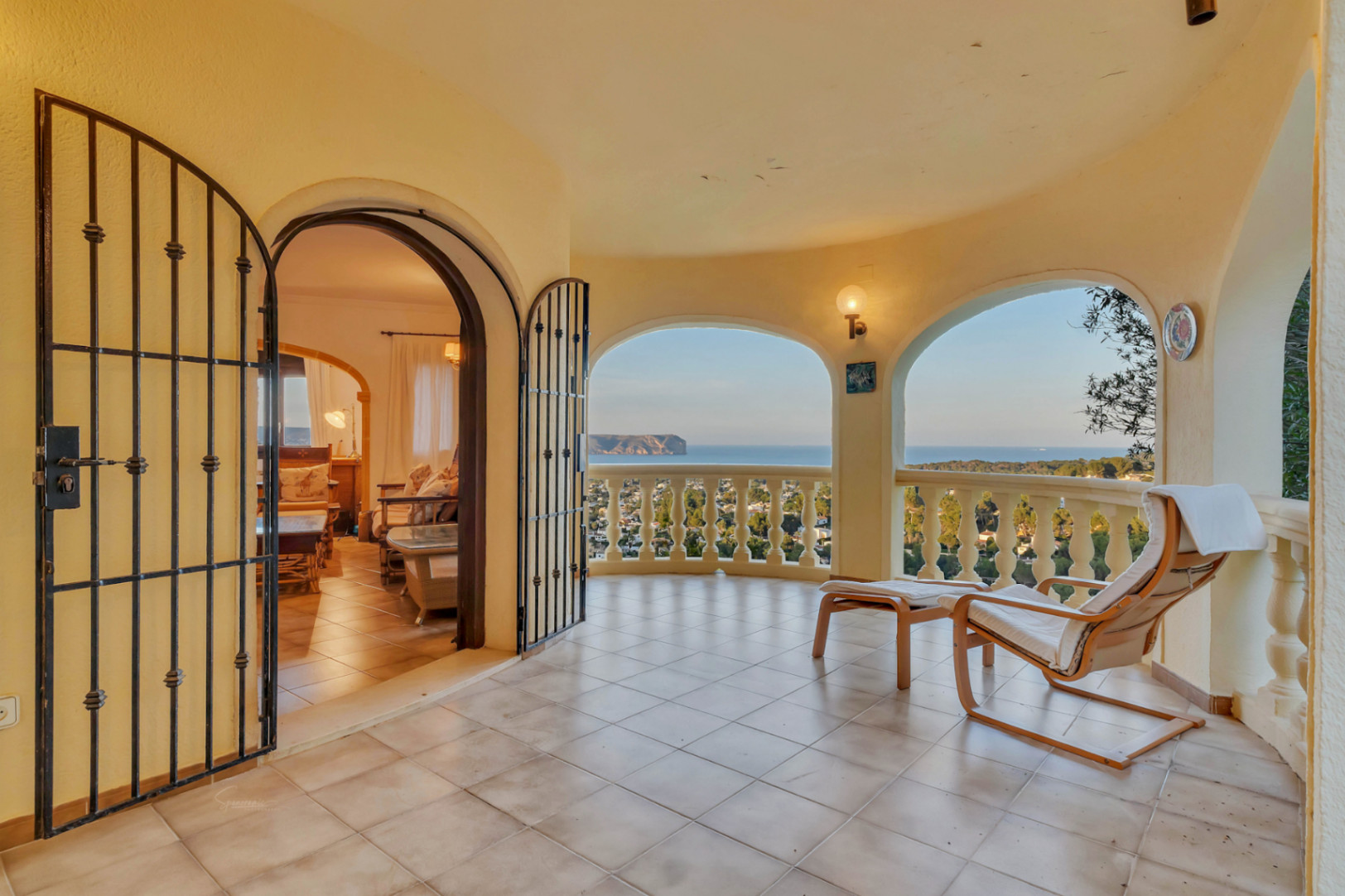 Covered terrace featuring arched openings, tiled flooring, and panoramic sea views. Wrought iron gates lead into the interior living space.