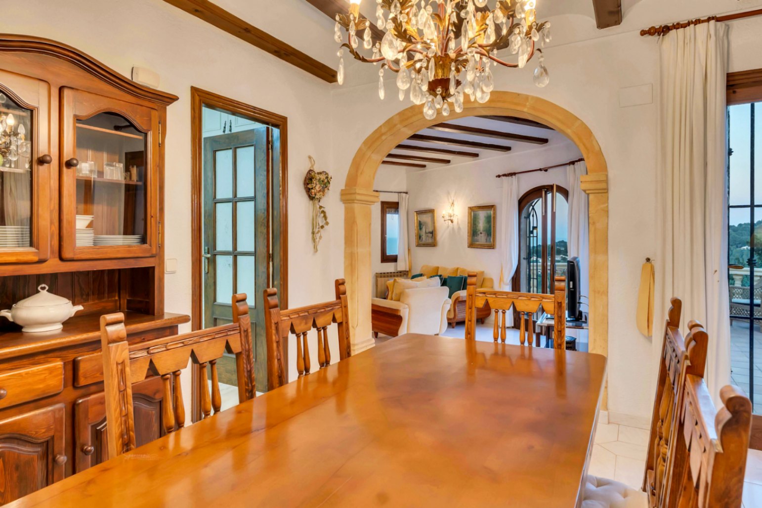 Dining area featuring solid wood furniture, exposed ceiling beams, and a traditional Tosca stone arch leading to the living room and terrace.