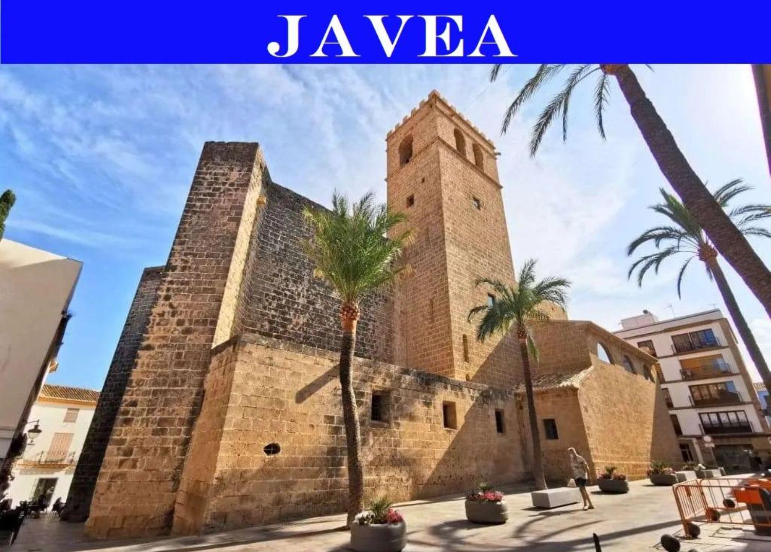 Exterior view of the historic San Bartolomé Church in Jávea's old town, featuring traditional Tosca stone architecture and a square bell tower flanked by palms.