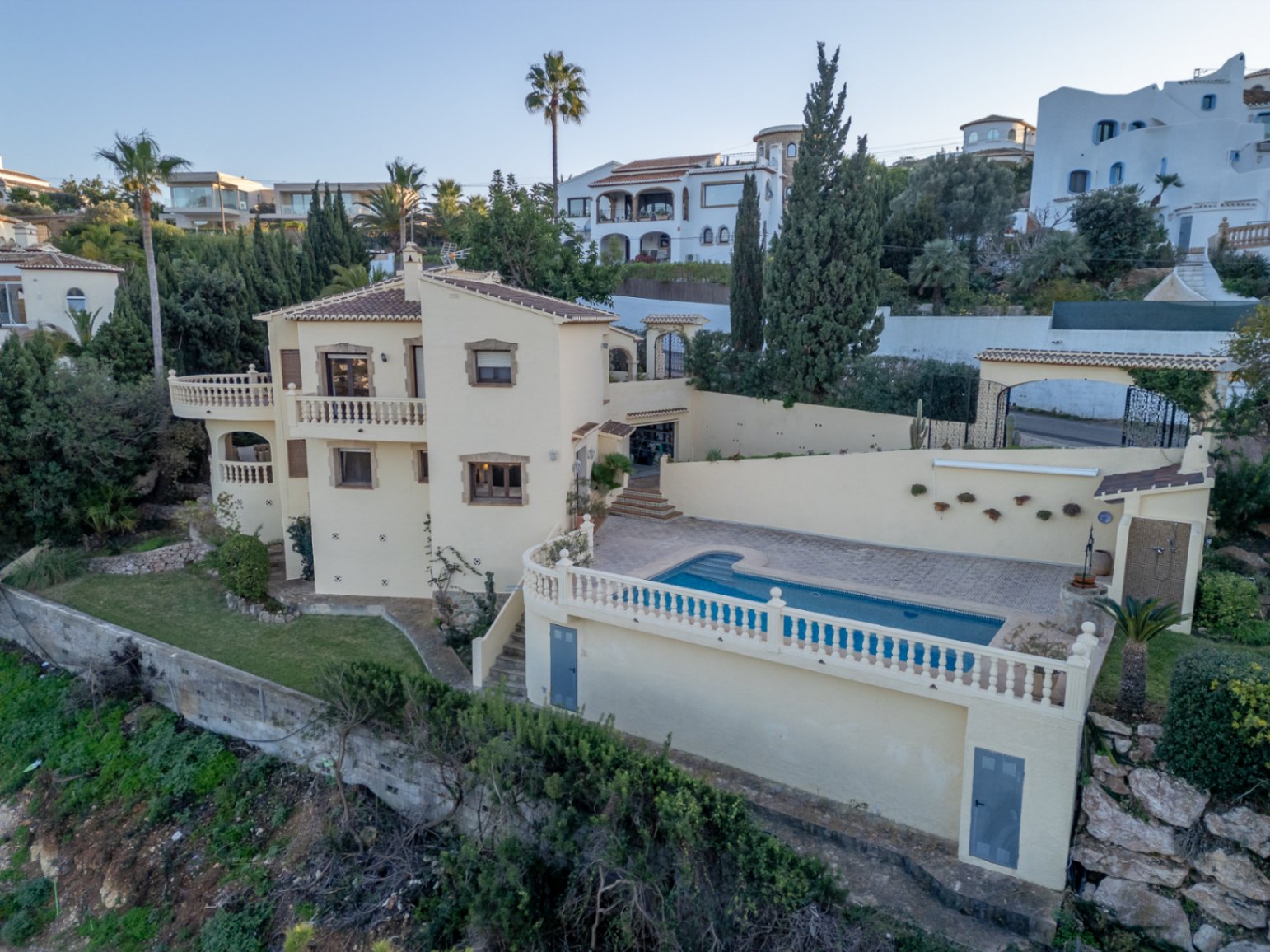 Exterior view of the Mediterranean villa featuring a private pool area, multiple terraces with white balustrades, and a cream facade with stone accents.