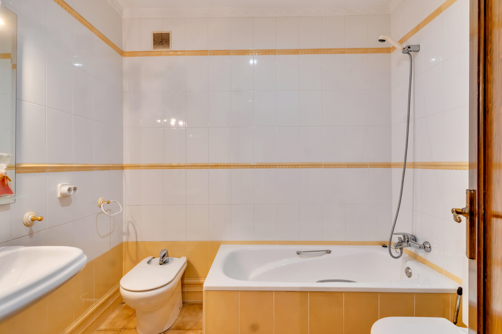 Functional bathroom featuring a built-in bathtub, bidet, and white wall tiling accented by decorative yellow borders and chrome fixtures.