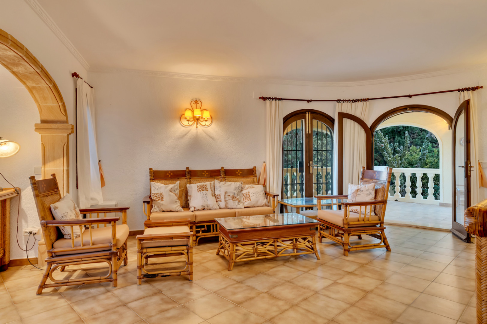Lounge featuring bamboo furniture, ceramic tile flooring, and a traditional Tosca stone arch. Arched wooden doors open onto a terrace with a white balustrade.