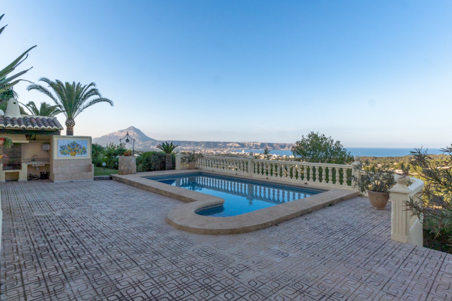 Outdoor pool area with Roman steps and tiled terrace, featuring a classic stone balustrade and panoramic views of Jávea Bay and the Montgó mountain.