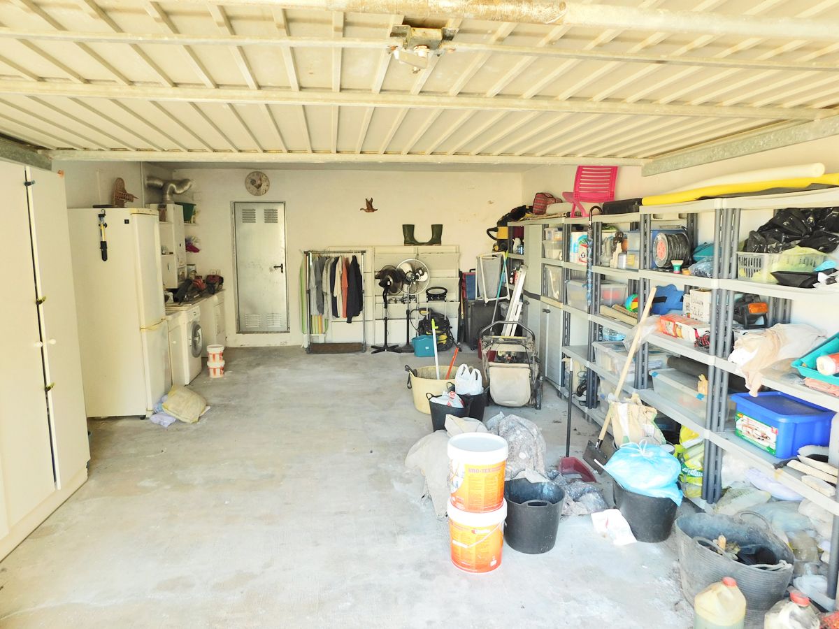Spacious double garage featuring a laundry area, extensive storage shelving, space for auxiliary appliances, and a durable concrete floor.